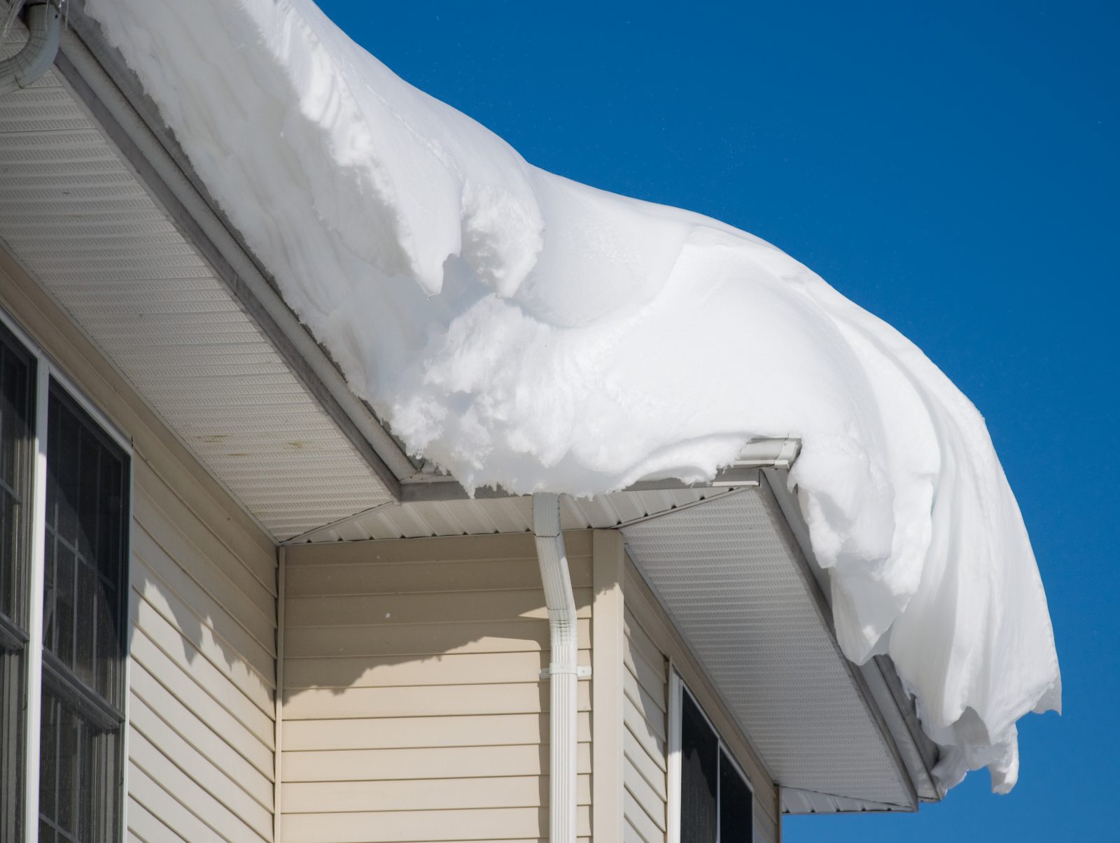 Accumulation de neige sur le toit d'une maison, nécessitant un déneigement pour éviter les dommages, par Zoom Toiture.